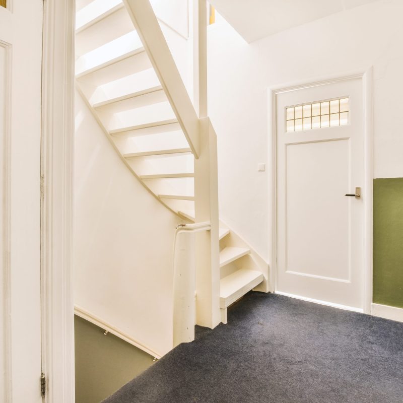 White hallway with wooden stairway leading to second floor of modern luxury apartment with minimalist interior design